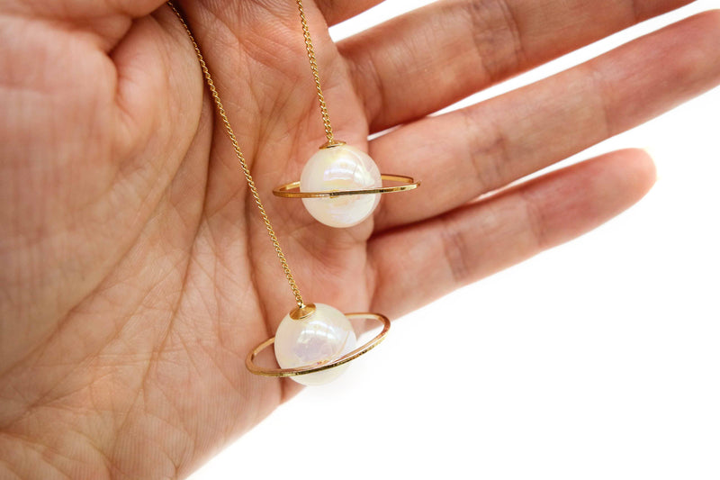 pearlescent white planet earrings in hand